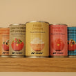 Four small cans of Nicola Fried Onion in Olive oilother sauces lined up on a wooden shelf against a beige wall. The cans feature colorful labels for various tomato-based and onion-based fried foods.