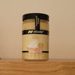 A jar of Nicola Fried Onion spread sitting on a wooden shelf against a plain beige wall.