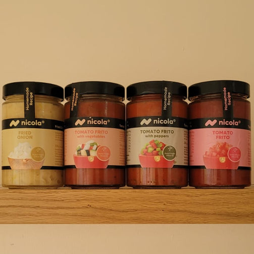 Four jars of Nicoça jam arranged on a wooden shelf against a plain beige wall. The jars contain different colored tomato frito sauces beige, reddish-brown, and pinkish-red, with black lids and white labels featuring the Nicola brand.