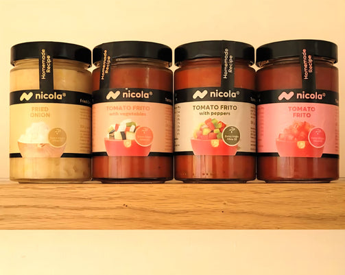 Four jars of Nicola brand homemade tomato Frito sauces and condiments lined up on a wooden shelf against a cream-colored background. The jars contain various tomato-based and onion-based sauces and feature black lids with white labels.